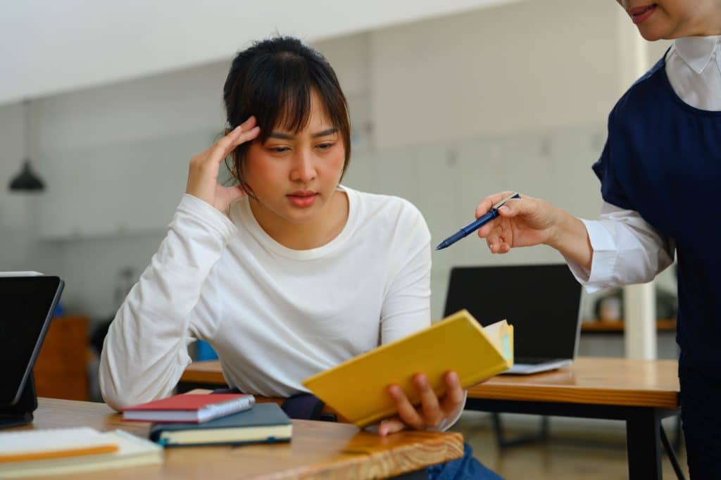 Mature lecturer helping female student struggling with schoolwork in a classroom