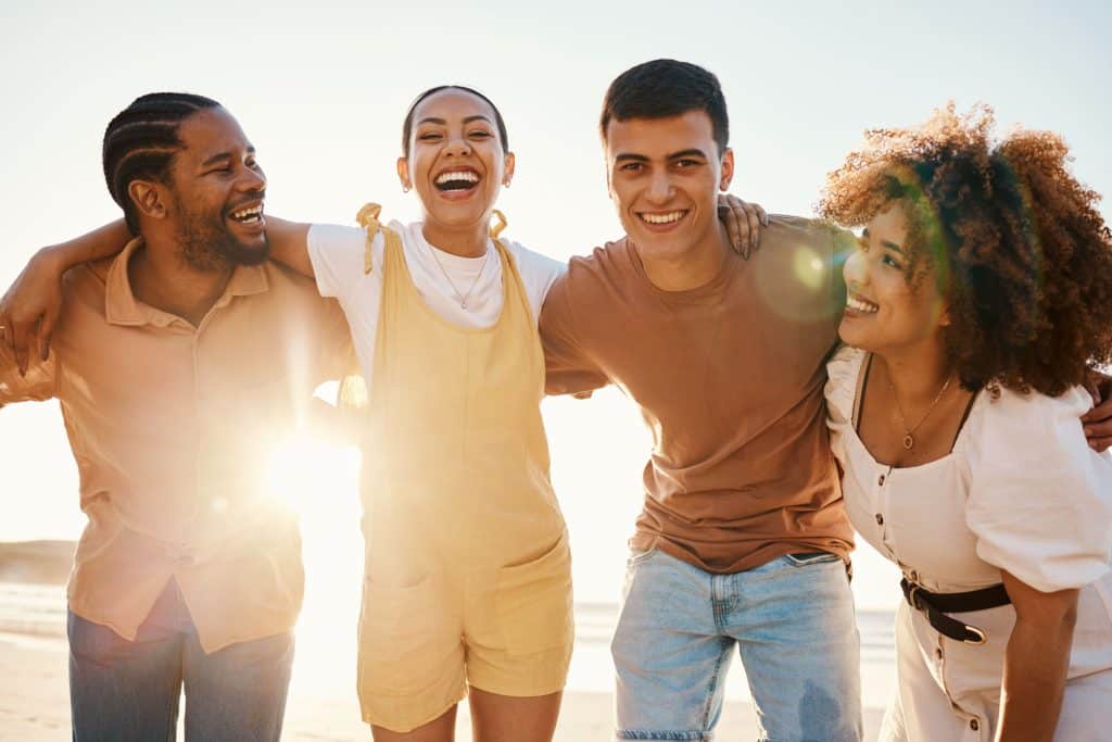 Beach sunset, happy and group of friends hug, smile and enjoy