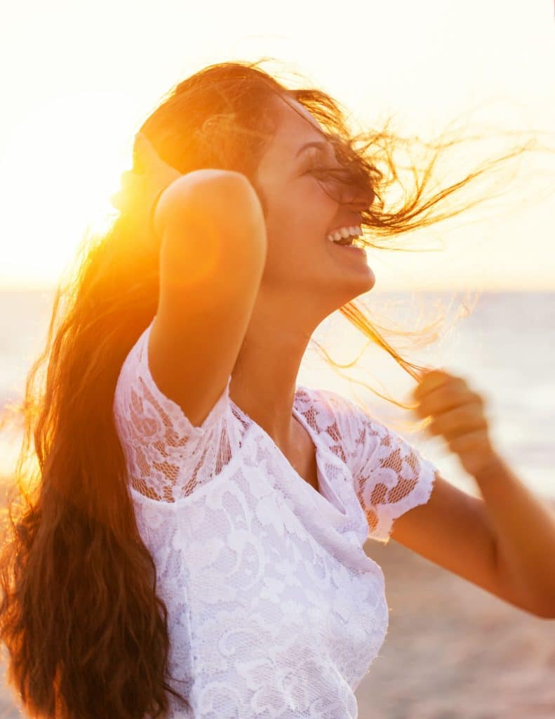 Beautiful young teenager with a white dress on the beach at sunset.