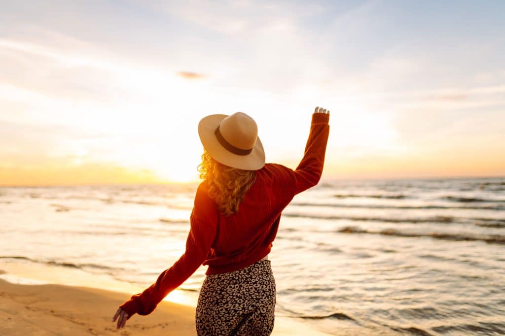 Stylish woman walks at sunset along beach of sea on at sunset. Travel, relax and lifestyle concept.